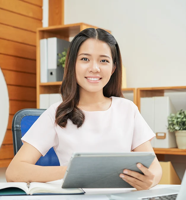 Office worker holding a tablet and smiling at her desk in a modern workplace