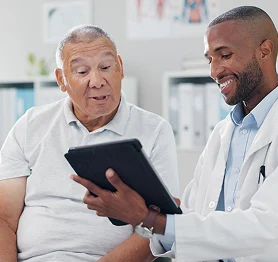 Doctor explaining test results to an elderly man using a digital tablet in a medical office.