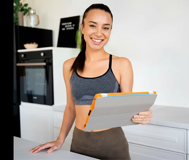 Smiling young woman in workout clothes holding a tablet in a modern kitchen